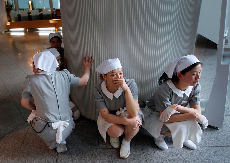 Работницы отеля в ужасе сидят у входа в отель в Токио. (Itsuo Inouye/Associated Press)