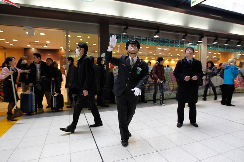 Работник станции Синагава руководит движением пассажиров после 
землетрясения в Токио. (Hiro Komae/Associated Press)