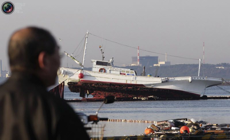 Человек смотрит на рыболовецкое судно, пострадавшее из-за цунами в порту города Оарай, на северо-восток от Токио, 12 марта 2011 года