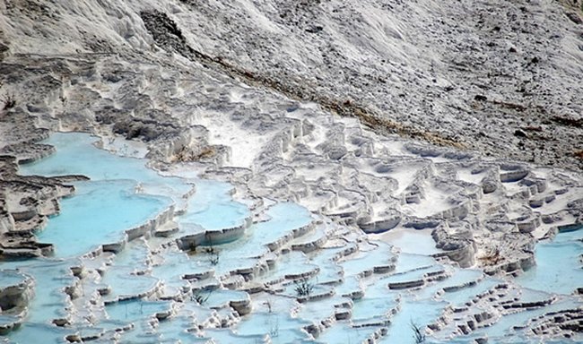 Вода, стекающая со склонов горы образует систему причудливых водоёмов с известняковыми стенами (травертинами). Ослепительно белые террасы (травертиновые образования) возникли на склоне горы в результате отложения солей из насыщенных кальцием источников. Раньше по соляным террасам разрешалось гулять босиком, но из-за многочисленности туристов, ежегодно посещающих Памуккале, это запретили. Теперь можно гулять по тропинке или любоваться великолепным зрелищем издали. Эти места используются как курортная местность с античных времен. В 1988 Памуккале и руины города Гиераполиса включены в список Всемирного наследия ЮНЕСКО.<br><br>(Wiki) Вода, стекающая со склонов горы образует систему причудливых водоёмов с известняковыми стенами (травертинами). Ослепительно белые террасы (травертиновые образования) возникли на склоне горы в результате отложения солей из насыщенных кальцием источников. Раньше по соляным террасам разрешалось гулять босиком, но из-за многочисленности туристов, ежегодно посещающих Памуккале, это запретили. Теперь можно гулять по тропинке или любоваться великолепным зрелищем издали. Эти места используются как курортная местность с античных времен. В 1988 Памуккале и руины города Гиераполиса включены в список Всемирного наследия ЮНЕСКО.<br><br>(Wiki)