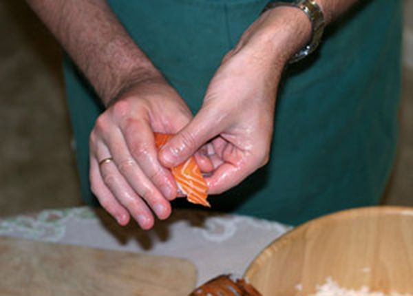 Осторожно переверните нигири, чтобы оно оказалось на кончиках пальцев левой руки рыбой кверху. Теперь переместите его к основанию пальцев, одновременно сжимая с торцов. Прижмите плотнее рыбу к рису.