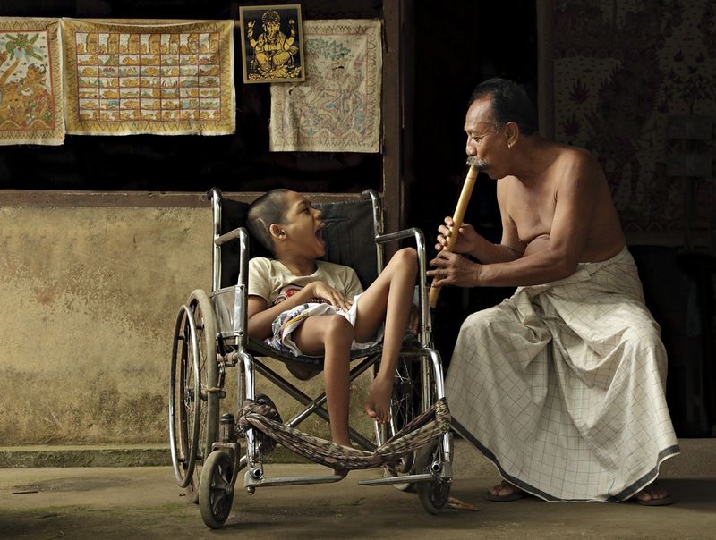 Музыка любви. Это фото было сделано в поселке Тенганан, Бали (в 2010 году). Тенганан – самый знаменитый поселок Бали, расположенный недалеко от Канди Даса в Восточном Бали. Мужчина играет на бамбуковой флейте, чтобы повеселить ребенка-инвалида. Это не его сын, хоть он и любит его как родного. (Photo and caption by Ario Wibisono)