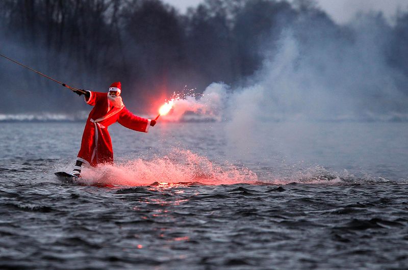 Мужчина в костюме Санта-Клауса с дымовой шашкой едет на вейкборде по небольшому озеру в Гамбурге 5 декабря.