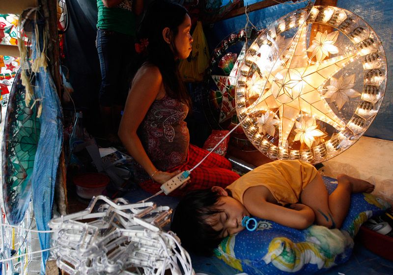 Девушка проверяет гирлянды на рождественском украшении рядом со своим спящим сыном в торговой палатке на улице Манилы 11 декабря. Филиппинцы празднуют один из самых длинных рождественских сезонов в мире, который начинается 16 декабря и заканчивается Крещением в январе. 