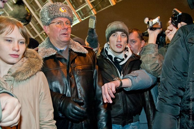 Действия Арзуманяна на Киевской прикрывает сотрудник милиции в штатском (человек с часами и перстнем). Вот фотография, на которой этот человек достает свое служебное удостоверение, чтобы его случайно не задержали ОМОНовцы.